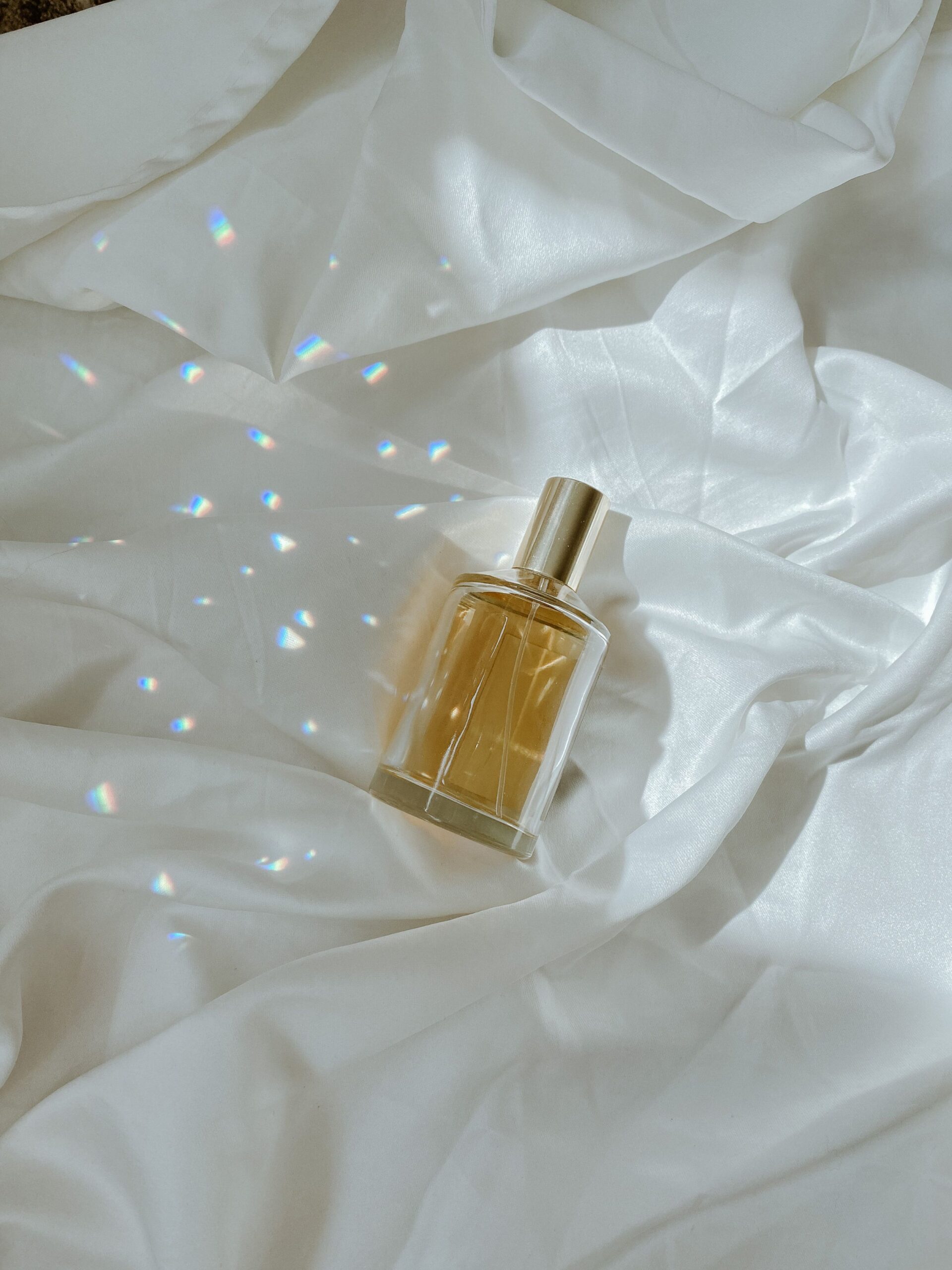 Glass perfume bottle on white silk with light prisms