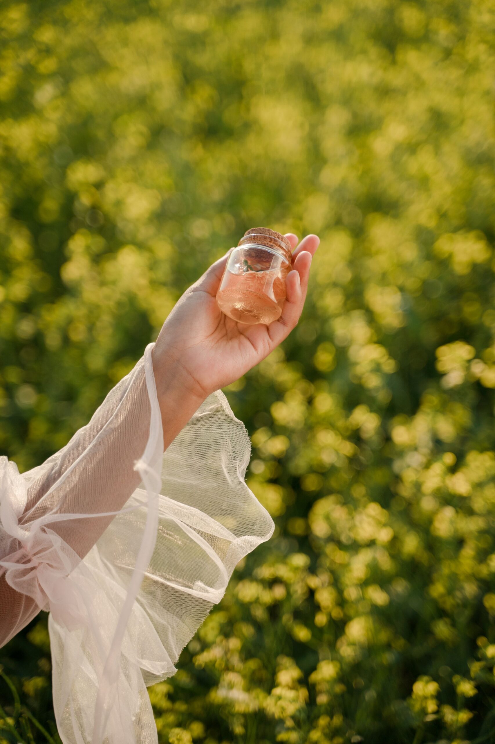 Hand holding a small glass jar against green foliage